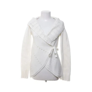 Vit omlottkofta från Bondelid - Superfin vit stickad omlottkofta från Bondelid med bred krage och knytband i midjan. Koftan har lång ärm och ett diskret hålmönster som ger en snygg detalj. Perfekt för lager-på-lager och mysiga dagar.