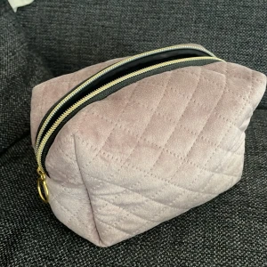 Necessär  - Säljer en necessär med mjuk lila utsida och svart insida samt dragkedja. Den är tvättad men har fortfarande några sminkfläckar på insidan som inte går bort, den har även tyvärr 2 små sminkfläckar på utsidan men det är inget man tänker på, se bild 2 och 3 för fläckarna! 