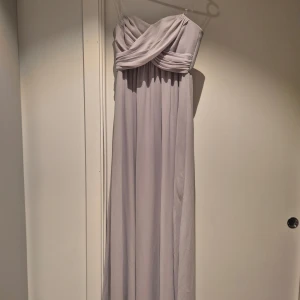Ljusgrå axelbandslös klänning H&M 34 - Elegant ljusgrå axelbandslös klänning från H&M. Klänningen har en vacker draperad överdel och är tillverkad i polyester. Använd 1 gång. Säljer då den har blivit för tajt på mig. 