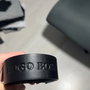 Svart bälte från Hugo Boss - Säljer ett svart bälte från Hugo Boss med präglad logga längs hela bältet och metallspänne med BOSS-gravyr. Bältet är stilrent och passar perfekt till jeans eller kostymbyxor. Materialet är skinn och spännet är i silverfärgad metall.