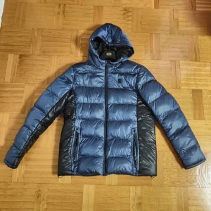 Mörkblå Dunnjacka, Storlek L - Elegant blå Dunnjacka från varumärket Blend med svarta detaljer, Håller dig varm och den är väldigt bekväm, Storlek L, Bra skick inga skador/slitage, PRIS KAN DISKUTERAS 