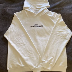 Vit hoodie från Maison Margiela - Säljer en oanvänd stilren vit hoodie från Maison Margiela. Hoodien har en klassisk design med långa ärmar och en bekväm huva. Perfekt för en avslappnad look. Skick 10/10