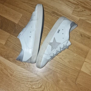 Vita sneakers med stjärndetalj - Snygga vita sneakers med en grå stjärna på sidan och grå snörning. Skorna har en klassisk design med en låg profil och en bekväm sula. Perfekta för en avslappnad stil. Saknar en bokstav och en stjärna 