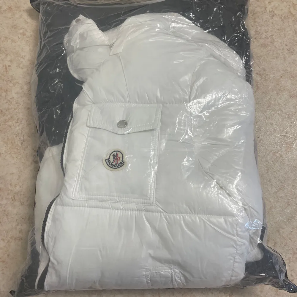Säljer en snygg vit dunjacka från Moncler med huva och dragkedja. Jackan har en bröstficka med knapp och Moncler-logga. Perfekt för kyliga dagar!. Takit.