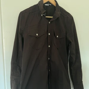 Brun skjorta från Vailent - Säljer en brun skjorta från Vailent med långa ärmar och knappar framtill. Skjortan har två bröstfickor med lock och knappar, vilket ger en stilren look. Perfekt för en avslappnad stil.