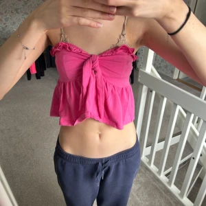 Rosa croppad topp - Säljer en söt rosa croppad bandeautopp med knytning framtill. Toppen har volangdetaljer som ger en romantisk touch. Perfekt för varma sommardagar!