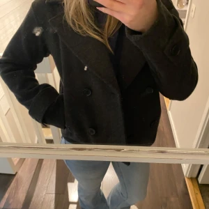 Mörkgrå kappa från Kappahl - Säljer en stilren mörkgrå kappa från Kappahl. Den har en klassisk dubbelknäppt design med breda slag och långa ärmar. Den är i storlek Xs och är endast provad, alltså i nyskick. Nypris är 999 kr, säljes för 699kr men kom gärna med prisförslag! Perfekt för inför våren🩷