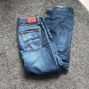  Nudie Jeans - Säljer ett par snygga blå jeans från Nudie Jeans. De har en klassisk femficksdesign med orange sömmar och en läderpatch baktill. Perfekta för en avslappnad stil. Steady Eddie