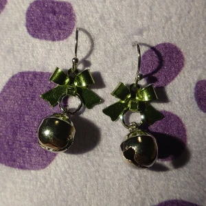 Örhängen med gröna rosetter och bjällror - Charmiga örhängen med gröna rosetter och silverfärgade bjällror. Perfekta för att ge en festlig touch till din outfit. Bjällrorna gör ljud! Inte använda.