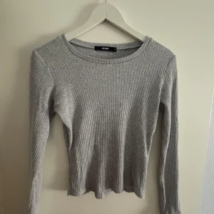 Grå ribbad tröja från Bik Bok - Säljer en stilren grå ribbad tröja från Bik Bok. Tröjan har en rund halsringning och långa ärmar, perfekt för en avslappnad look. Passar bra till både jeans och kjol. 🖤