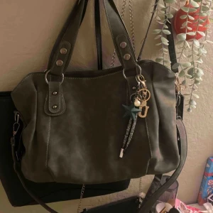 Grön axelväska med detaljer - Snygg grön axelväska i mocka liknande material🌸 dekorativa detaljer och avtagbar axelrem. Väskan har flera fack och en dragkedja för säker förvaring. 