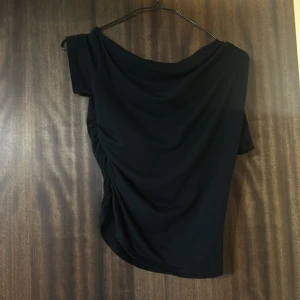 Svart offshoulder topp - Snygg svart offshoulder topp med draperad design på ena sidan. Perfekt för en stilren och elegant look. Passar bra till både jeans och kjol.