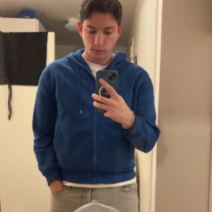 Blå hoodie med dragkedja - Säljer en snygg blå hoodie med dragkedja. Perfekt för en avslappnad stil. Den har långa ärmar och en bekväm passform.