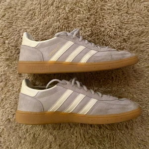 Grå Adidas Spezial sneakers - Snygga grå Adidas Spezial sneakers med klassiska vita ränder och gummisula. Skorna har snörning och är tillverkade i mocka med en rund tå. Perfekta för en stilren och sportig look.