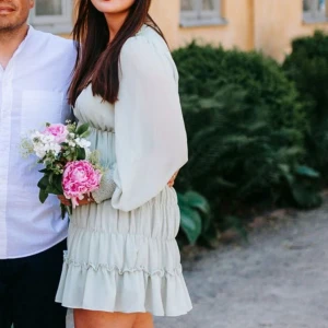 Ljusgrön klänning med volanger - Säljer en söt ljusgrön klänning med volanger och v-ringning. Klänningen har långa ärmar med smockdetaljer vid ärmsluten. Perfekt för vår och sommar!