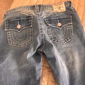 Blå jeans från True Religion - Snygga blå jeans från True Religion med broderade detaljer på bakfickorna. De har en bootcut-stil och är tillverkade i jeansmaterial. Perfekta för en avslappnad look med en touch av stil. Aldrig använda. Köpte fel storlek. Långa i benen. 