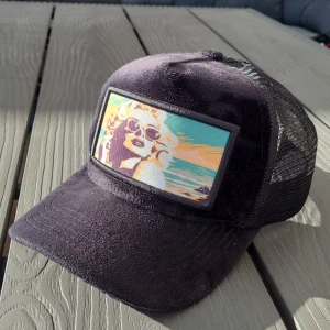 Svart keps med tryck från Revenite - Cool svart keps från Revenite med ett färgglatt tryck av en person i solglasögon. Kepsen har ett nätmaterial på baksidan för ventilation och justerbar passform. Perfekt för en avslappnad stil.