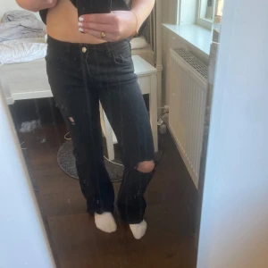 Svarta jeans med slitningar - Snygga svarta jeans från h&m med slitningar på knäna för en trendig look. De har en dragkedja och knapp framtill. Perfekta för en avslappnad stil. Köpte av någon som gjorde hålen själv. Fina och lågmidjade med silver detaljer 💞