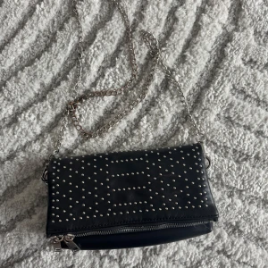 Svart axelväska med nitar - Snygg svart axelväska med silverfärgade nitar och kedja, den är dock lite lite rostig på kedjan.Perfekt för att ge din outfit en edgy touch. Väskan har en dragkedja för säker förvaring.