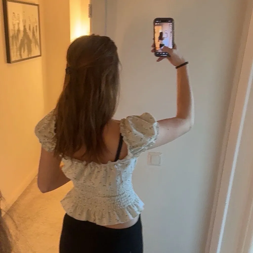 Blommig ljusgrön topp med volangdetaljer och knytning framtill. Toppen har korta ärmar och en smockad midja som ger en fin passform. Perfekt för en somrig look! Toppen är endast använd en gång.. Yläosat.