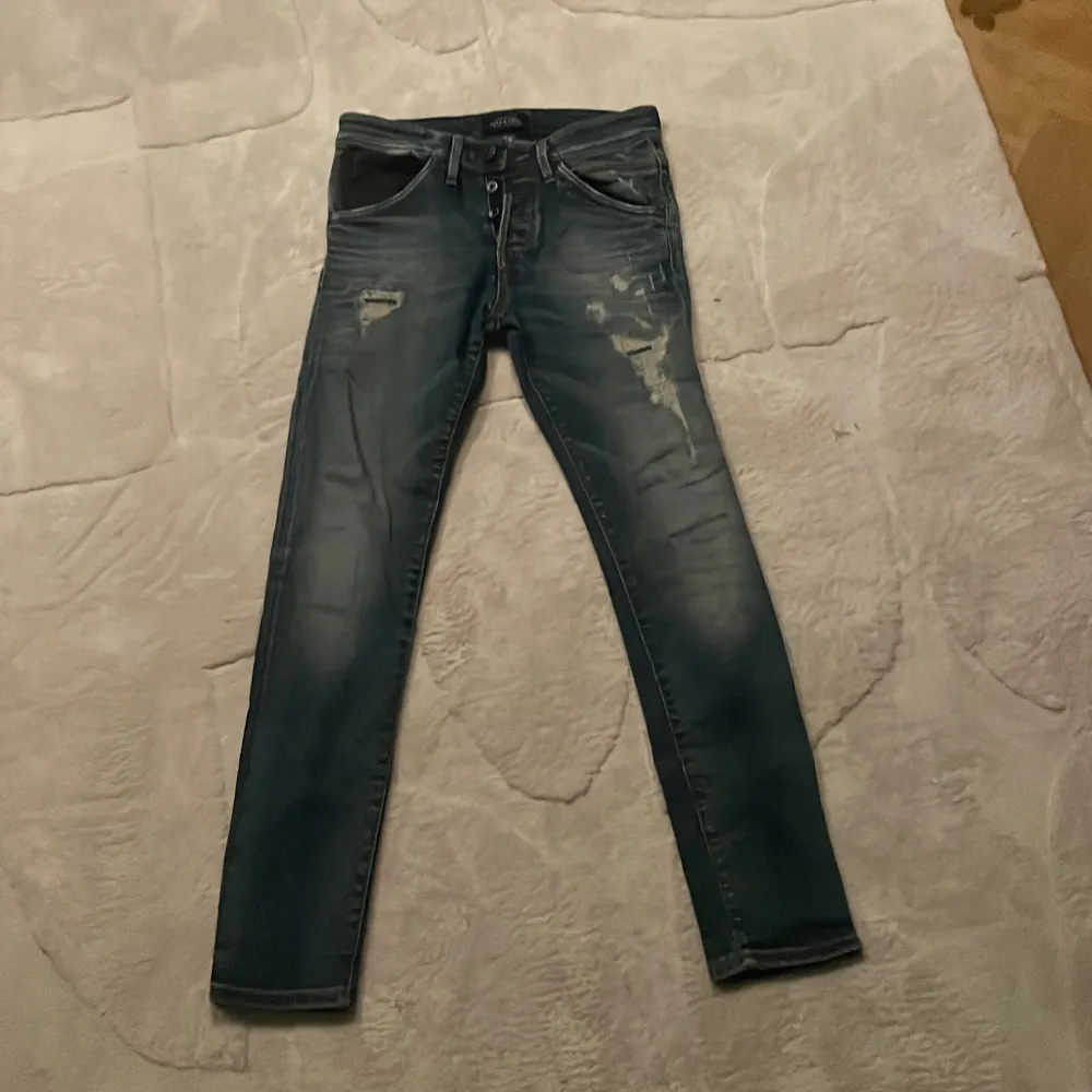 Snygga blå slim fit jeans från Jack & Jones med slitna detaljer. Perfekta för en avslappnad stil. Modellen heter Glenn och har en modern passform.. Farkut & Housut.