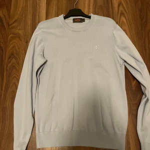 Ljusblå tröja från Morris - Köptes i för 1200kr. Storlek L och knappt använt. Stilren ljusblå tröja från Morris i 100% Pima Cotton. Tröjan har en liten broderad detalj på bröstet och ribbade kanter vid ärmslut och nederkant. Perfekt för en avslappnad och snygg look. 