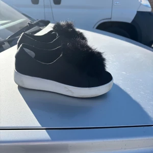 Svarta sneakers med pälsdetalj från Steve Madden - Snygga svarta sneakers från Steve Madden med en unik pälsdetalj på ovansidan. Skorna har en vit sula som ger en cool kontrast och en modern look. Perfekta för att ge din outfit en extra touch av stil. 