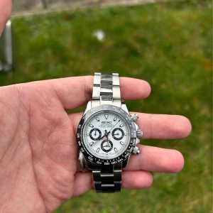 Seiko kronografklocka i silver - Säljer en snygg Seiko kronografklocka med en stilren silverfärgad boett och armband. Urtavlan är vit med tre sub-dials och svarta detaljer. Perfekt för den som gillar en klassisk och tidlös design.