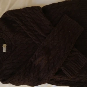 Mörkbrun stickad tröja - Säljer en mysig mörkbrun stickad tröja med kabelstickat mönster. Tröjan har långa ärmar och ribbstickade muddar vid ärmslut och nederkant. 