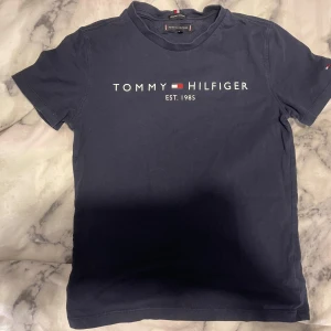 Mörkblå t-shirt från Tommy Hilfiger - Säljer en snygg mörkblå t-shirt från Tommy Hilfiger med deras ikoniska logga och text 'EST. 1985' på framsidan. T-shirten har en klassisk rund hals och korta ärmar. Den är använd någon enstaka gång men har inga defekter😊