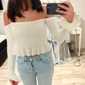 Vit ribbad offshoulder topp - Säljer en stilren vit ribbad offshoulder topp med långa ärmar och volangdetaljer vid ärmslut och nederkant. Perfekt för en trendig look!