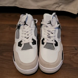 Nike Air Jordans i vit och grå - Snygga Nike Air Jordans i vit och grå med svarta detaljer. Skorna har en klassisk design med snörning och meshpaneler för extra ventilation. Perfekta för både stil och komfort.