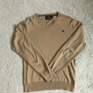 Beige v-ringad tröja från Morris - Säljer en stilren beige v-ringad tröja från Morris i 100% pima bomull. Tröjan har långa ärmar och en liten broderad logga på bröstet. Perfekt för en klassisk och avslappnad look.