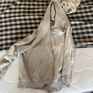 Grå hoodie med dragkedja - Säljer en klassisk grå hoodie med dragkedja och huva. Tröjan har långa ärmar, ribbade muddar och snörning i huvan. Perfekt för en avslappnad stil. Använd en del men endå i fint skick! 