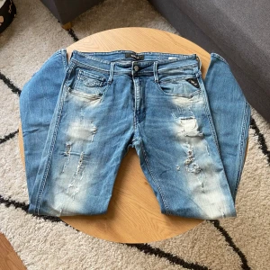 Blå slitna jeans från Replay - Hejsan👋 Säljer ett par blå jeans från Replay med slitningar och ljusa partier framtill i Anbass modell.👖  Klassisk femficksmodell med dragkedja och knapp. Snygga detaljer på bakfickorna och patch med Replay-logga i midjan🤩  Storleken är W32 L32!📐  Pris kan diskuteras vid snabb affär!💸  Vid frågor: Meddela📩