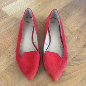 Röda mocka ballerinaskor med spetsig tå - Säljer ett par röda ballerinaskor i mocka från Tamaris. Skorna har spetsig tå och platt sula. Sanna i storleken. Tveka inte på att höra av vid frågor eller prisförslag!