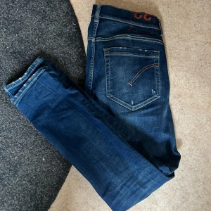 Dondup George - Snygga blå jeans från Dondup med slitna detaljer och en klassisk femficksdesign. De har en knappgylf och är perfekta för en avslappnad stil. Passformen är slim och de har en normal midja. Jeansen är i väldigt bra skick med väldigt snygga slitningar.Mitt pris 500kr nypris runt 3000kr. Pris går att diskutera. Kontakta mig om du har frågor.