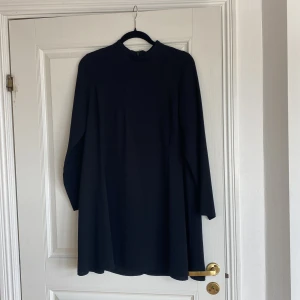Svart klänning med lång ärm från Gina Tricot - En stilren svart klänning från Gina Tricot med lång ärm och hög hals. Klänningen har en rak passform och dragkedja i ryggen. Perfekt för dig som gillar minimalistisk och klassisk stil. Svårt att få rätt svart, snyggare i verkligheten. Stl 40.