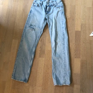 Ljusblå jeans från Gina Tricot - Säljer ett par ljusblå jeans från Gina Tricot i storlek 158. Jeansen har klassisk femficksdesign, raka ben och en liten sliten detalj på ena låret. Perfekta för en avslappnad och trendig look.