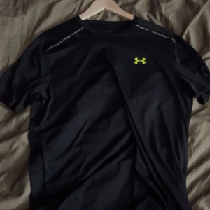 Under armour t shirt - Svart t-shirt från Under Armour med korta ärmar och logga i neongult på bröstet. Perfekt för träning med sportig design och bekvämt material.