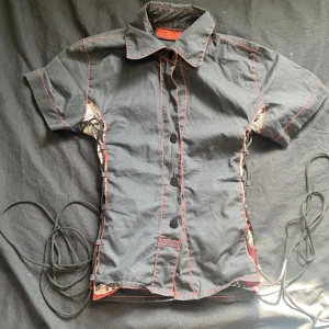 Svart skjorta med detaljer  - Jätte snygg skjorta knappast använd adjustbar med snörerna på sidan de är typ dödskalar o rosor på sidan skriv om ni undrar något köpt på xplosion