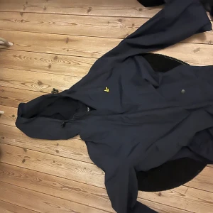 Mörkblå vindjacka med huva från Lyle & Scott - Säljer en mörkblå vindjacka med huva från lyle & scott. Jackan är köpt för 1500 och är i mycket bra skick.