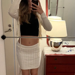 Vit stickad kortkjol - Säljer en vit stickad kortkjol med kabelstickat mönster och bred midjeresår. Kjolen är mjuk och passar perfekt till en trendig vardagslook. Enkel att matcha med olika toppar för en snygg outfit. Är i storlek 36 och är i super fint skick. Ifrån new Yorker.