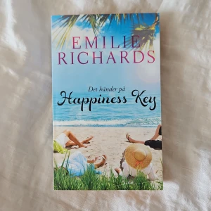 Det händer på Happiness Key - En roman om fyra kvinnor som möts på Happiness Key, en strandnära plats. Boken utforskar vänskap, hemligheter och nya möjligheter i livet. Omslaget visar en strand med palmer, blå himmel och kvinnor som vilar i sanden, vilket ger en somrig och avslappnad känsla.