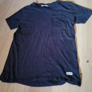 Svart t-shirt med bröstficka från lager 157 - En svart t-shirt från lager 157 i 100% bomull. T-shirten har en klassisk passform med korta ärmar och en liten bröstficka på vänster sida. Perfekt till vardags och enkel att matcha med det mesta. Den är ljusare än ny, men den är fortfarande svart. Lite ytludd finns 