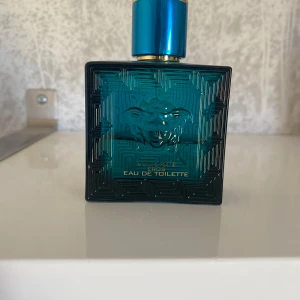 Versace Eros Eau de Toilette herrparfym - Versace Eros Eau de Toilette i en stilren turkosblå glasflaska med guldiga detaljer och ikoniskt Medusahuvud. Parfymen har en fräsch och maskulin doft, perfekt för dig som gillar exklusiva och moderna dofter.