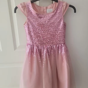 Glitter barnklänning - Fin glitter klänning för flickor, använd några gånger men passar väldigt fint på. Storlek 134. Klänningen är hämtad från polen.