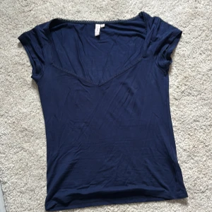 Mörkblå v-ringad topp - Säljer en mörkblå topp med v-ringning och korta ärmar. Enkel och stilren design, perfekt att matcha med jeans eller kjol. Tunt och mjukt material som känns skönt mot huden.