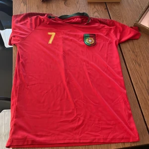 Röd fotbollströja med nummer 7 - Snygg röd fotbollströja från Nike med nummer 7 och namn på baksidan. Tröjan har korta ärmar och ett emblem på bröstet. Perfekt för fotbollsfans!