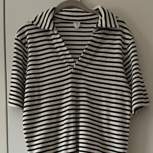 Randig frottétröja med krage & shorts - Säljer en vit och svart randig tröja i frotté med krage och v-ringning. Tröjan har korta ärmar och en avslappnad passform, perfekt för varmare dagar. Matchande shorts. Mjuk och skön mot huden.